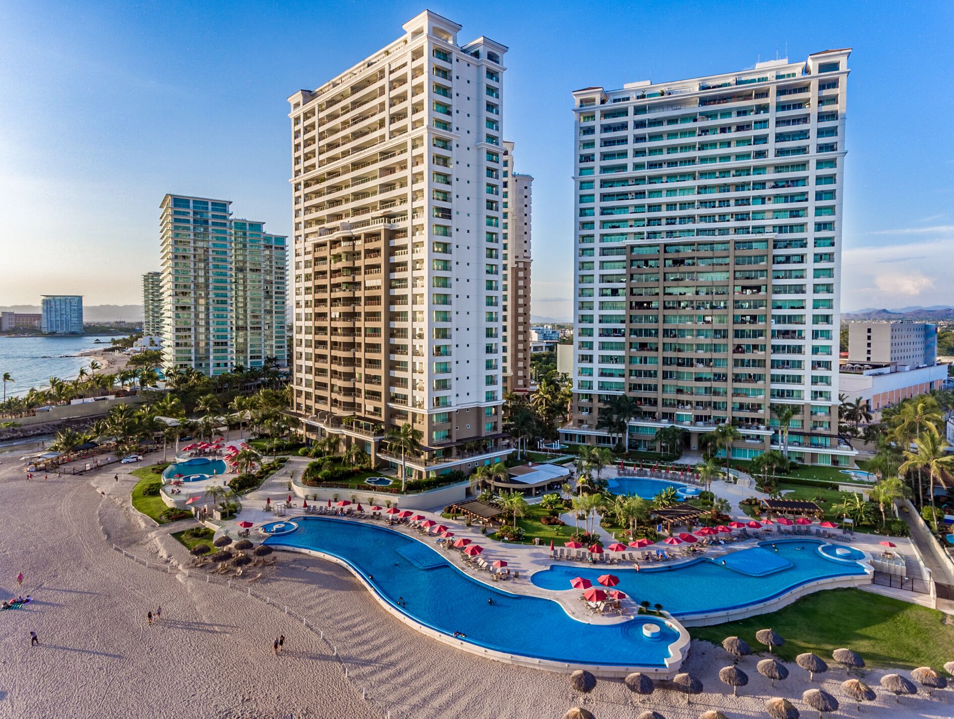 A high-rise hotel with multiple floors, a central swimming pool, and a beach area.