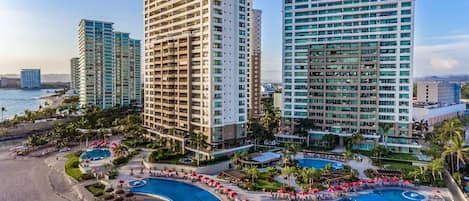 A high-rise hotel with multiple floors, a central swimming pool, and a beach area.