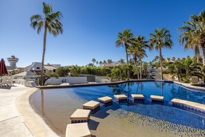 Une piscine bordée de palmiers, avec des chaises longues et un poste de surveillance pour les sauveteurs.