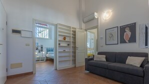 A room with a grey sofa, a white wardrobe, a bed with a window, and two framed pictures on the wall. - GuestHost - Manfredini Historical House in the heart of Ferrara (Ferrara)