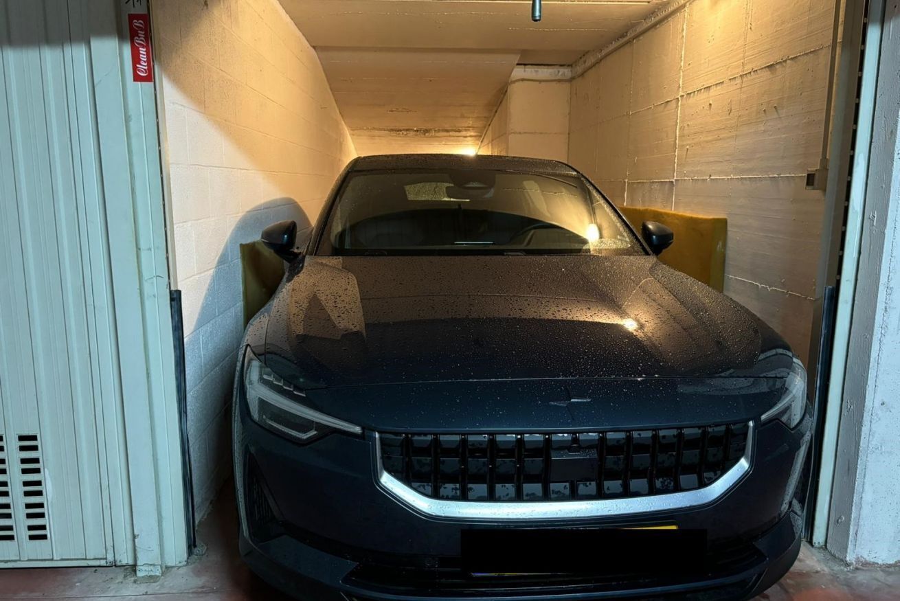 A black car parked in a narrow, enclosed space with concrete walls and a white door.