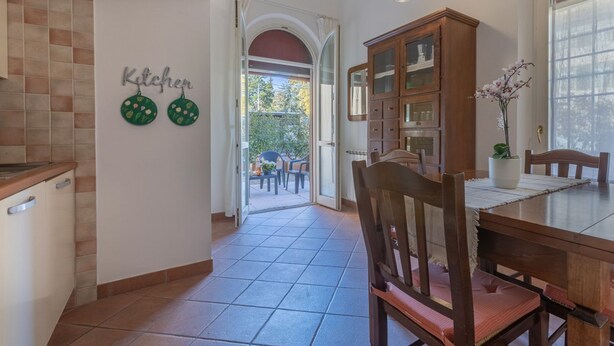 A kitchen with a 'Kitchen' sign, a dining area with a table and chairs, a wooden cabinet, and a view through an open door to an outdoor patio. - GuestHost - Manfredini Historical House in the heart of Ferrara (Ferrara)