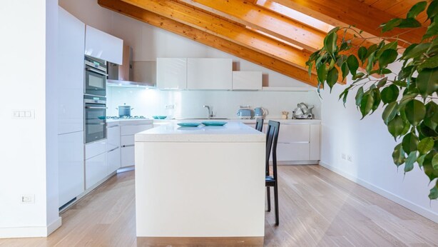 Een moderne keuken met witte kastjes, een centraal eiland en houten balken in het plafond.
