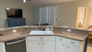 A corner kitchen with a dishwasher, white cabinets, a sink, and a TV mounted above the cabinets. - Charming 3-bedroom house in Englewood within minutes of beaches and golf. (Englewood)