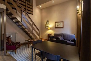 A modern living room with a staircase, a sofa, a dining table, and a lamp.
