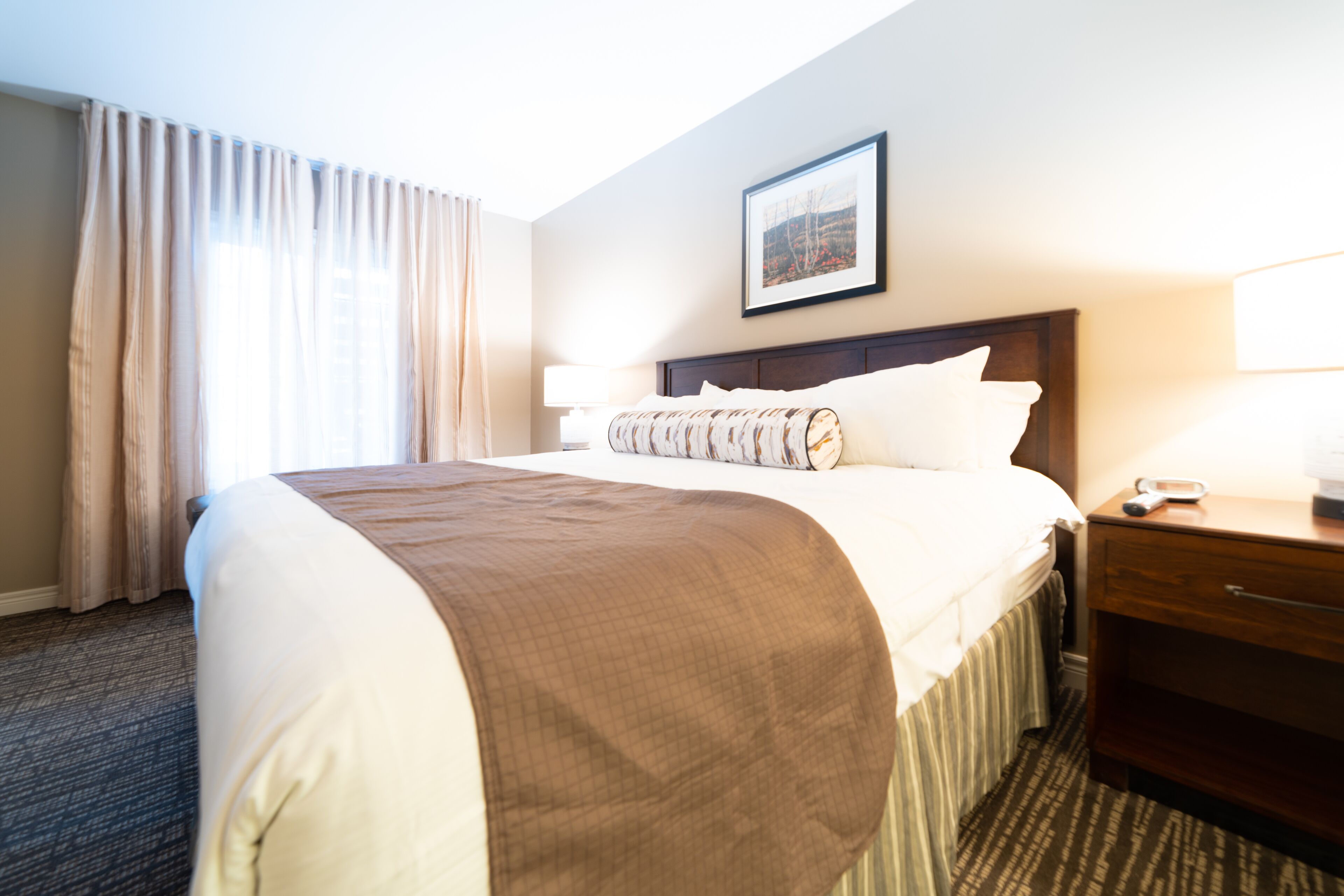 A hotel room with a large bed, a wooden nightstand, a lamp, and a framed picture on the wall.