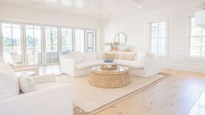 A spacious living room with a white sofa set, a round coffee table, and large windows offering a view of the outdoors. - Gulf Bridge by Stay on 30a (Inlet Beach)