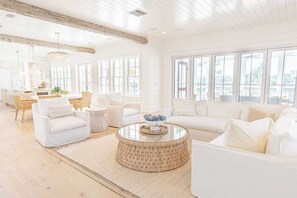 Ein geräumiges Wohnzimmer mit einer großen weißen Couch, einem runden Couchtisch und einem Essbereich mit einer Pendelleuchte.