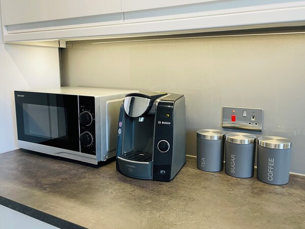 A kitchen with a microwave, a coffee maker, and three containers labeled tea, sugar, and coffee.