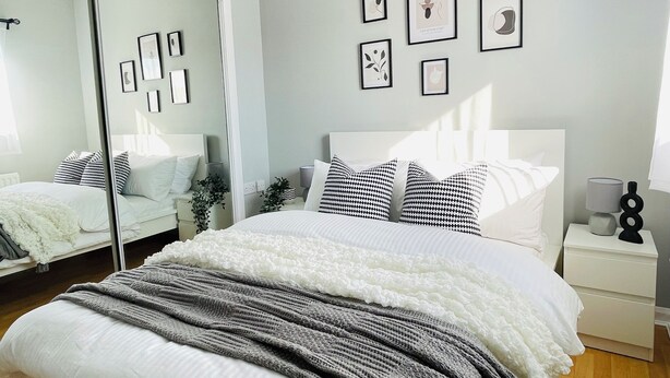 A modern bedroom with a large bed, a bedside table, a mirror, and wall-mounted artwork.