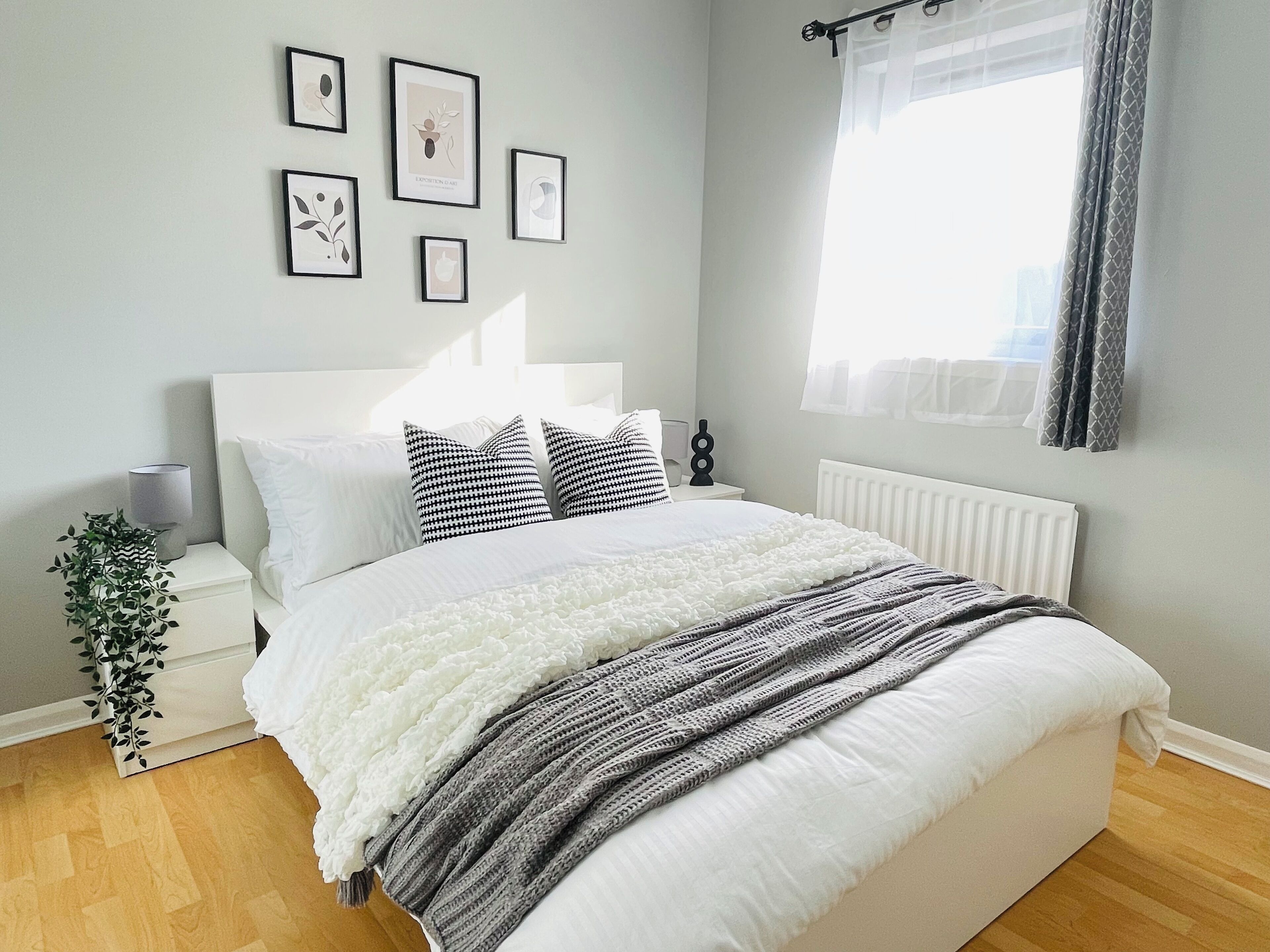 A neatly arranged bedroom with a bed, bedside tables, a potted plant, and framed artwork on the wall.