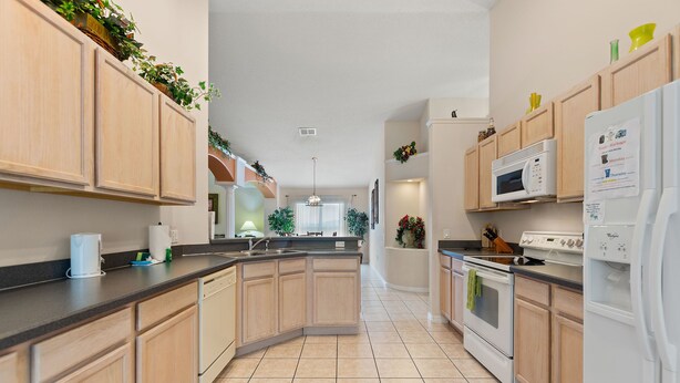 A modern kitchen with wooden cabinets, a central island, a microwave, an oven, and a refrigerator. - Soaring Eagle at Eagle Point by Shine Villas 102 (Kissimmee)