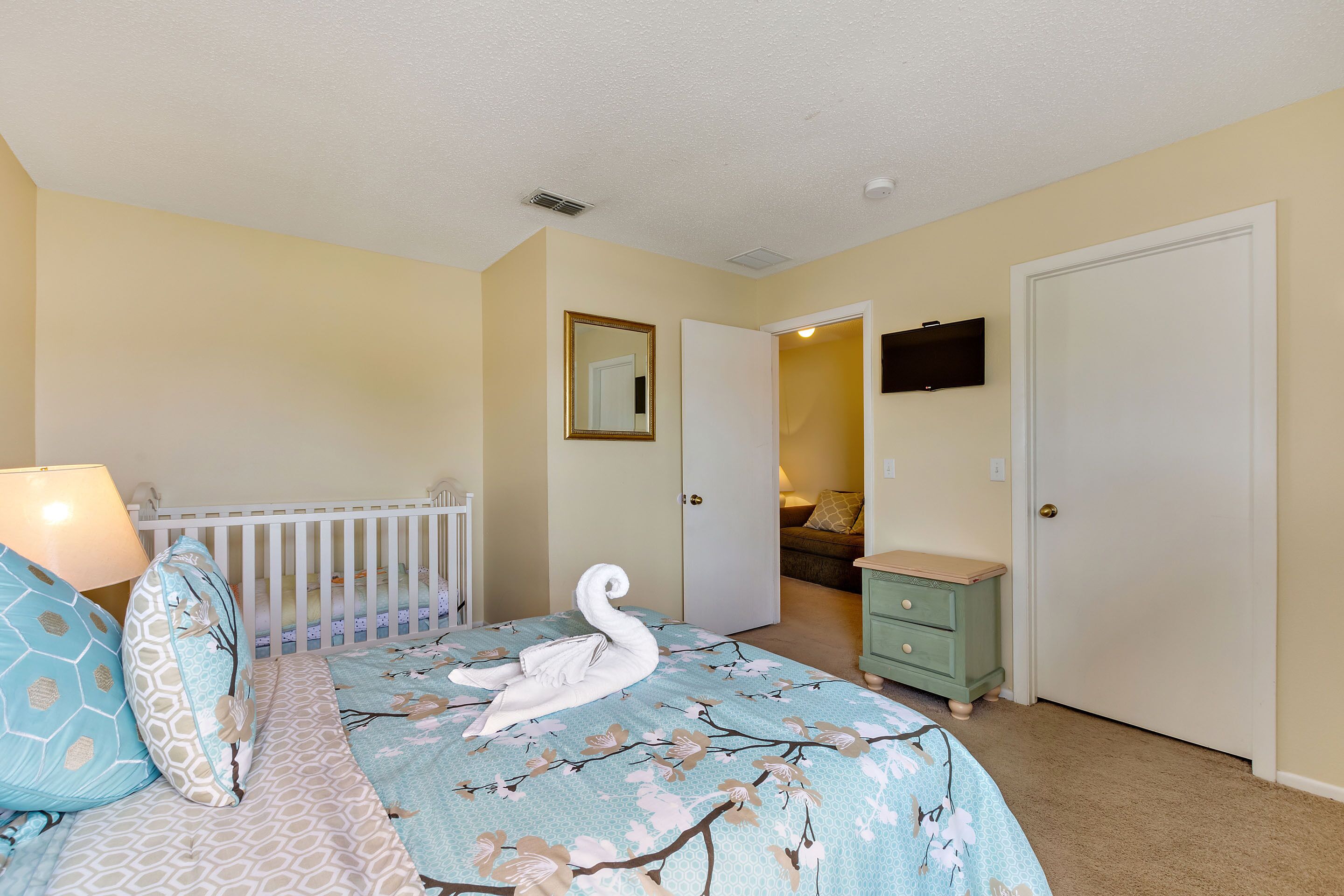A bedroom with a bed, a dresser, a door, and a crib.