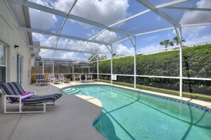 Una piscina interior con sillones de descanso, un patio cubierto y vistas a un jardín ajardinado.