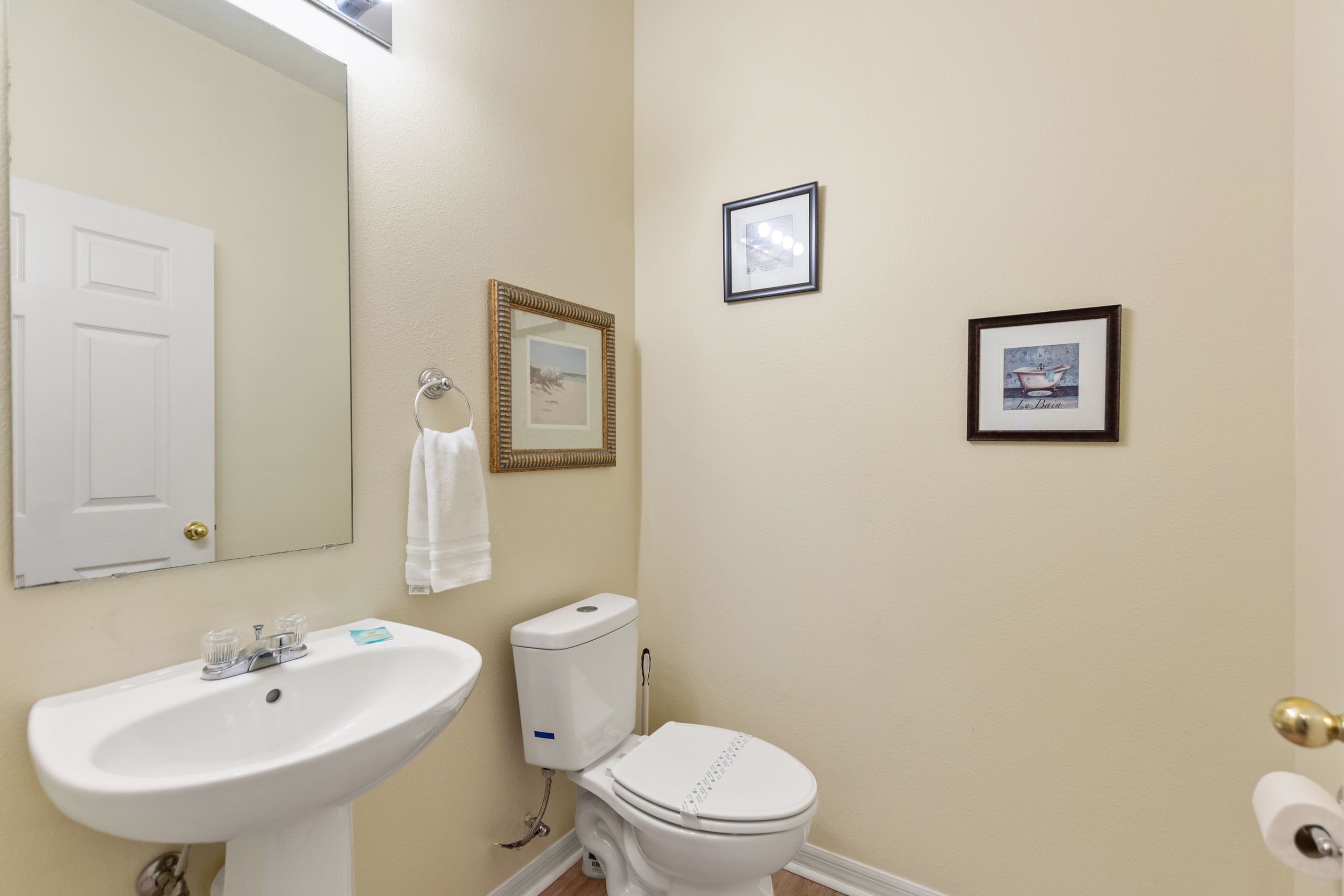 A bathroom with a white sink, toilet, and mirror. There are framed pictures on the wall.