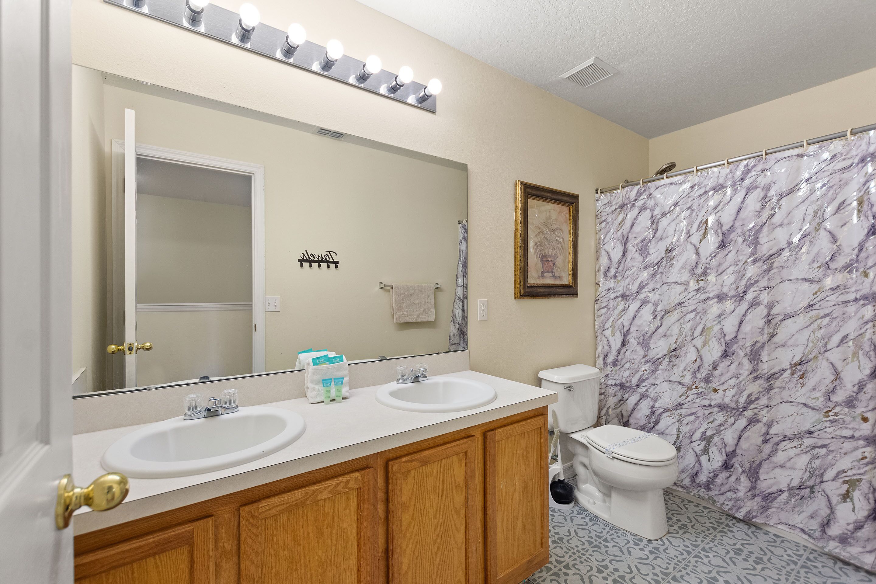 A bathroom with two sinks, a mirror with lights, a toilet, and a shower curtain.