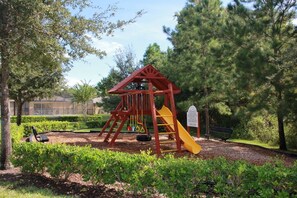 A playground with a red and yellow slide, surrounded by trees and a bench. - Tranquil Hideaway at Sandy Ridge (Davenport)