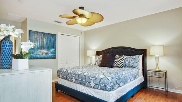 A bedroom with a bed, a ceiling fan, a painting, a vase with flowers, and a nightstand with a lamp. - Tranquil Hideaway at Sandy Ridge (Davenport)