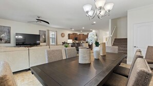 Un salon moderne avec une table à manger en bois foncé, des canapés de couleur beige et un grand téléviseur à écran plat.