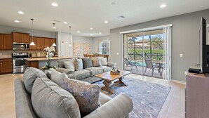 A spacious living area with a gray sofa, a wooden coffee table, and a large window offering a view of a swimming pool. - Blissful Haven @ Windsor Westside by Shine Villas 995 (Kissimmee)