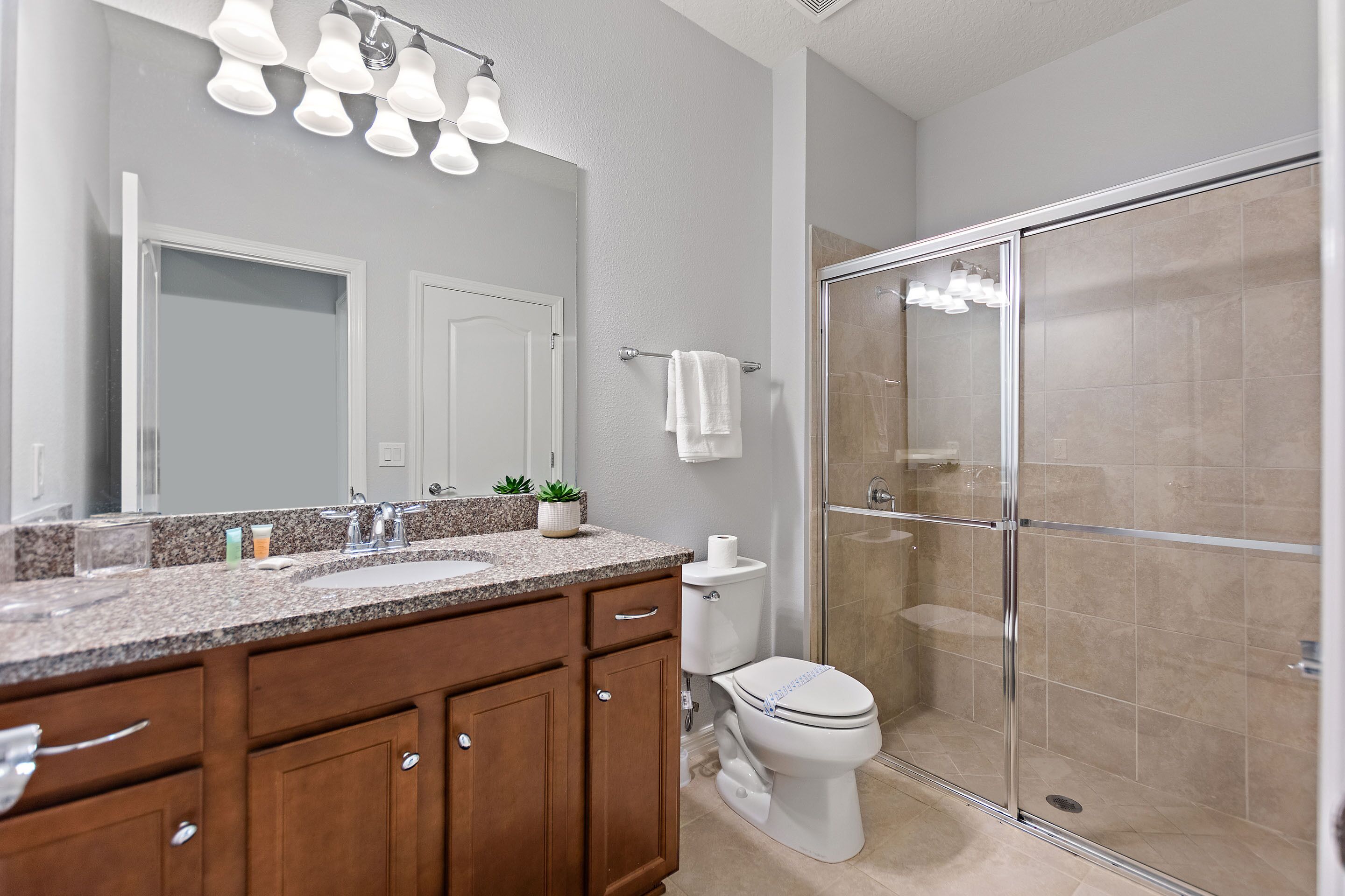 A bathroom with a granite countertop, wooden cabinets, a toilet, and a glass-enclosed shower.
