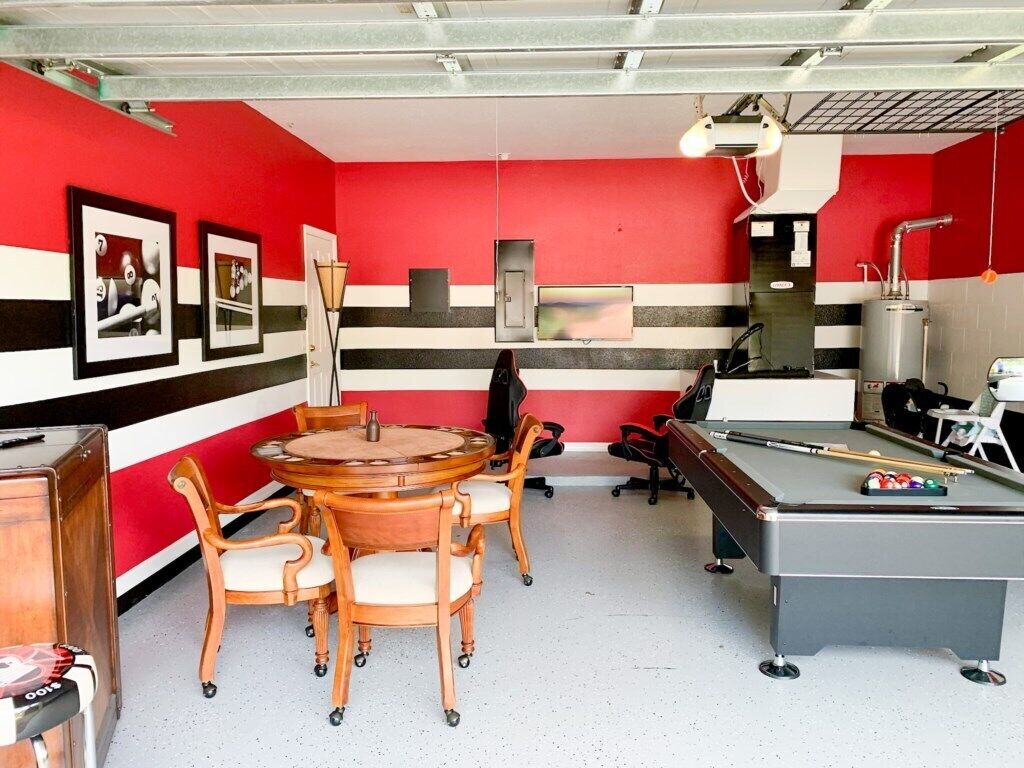 A room with a pool table, a billiards rack, and a table with chairs.