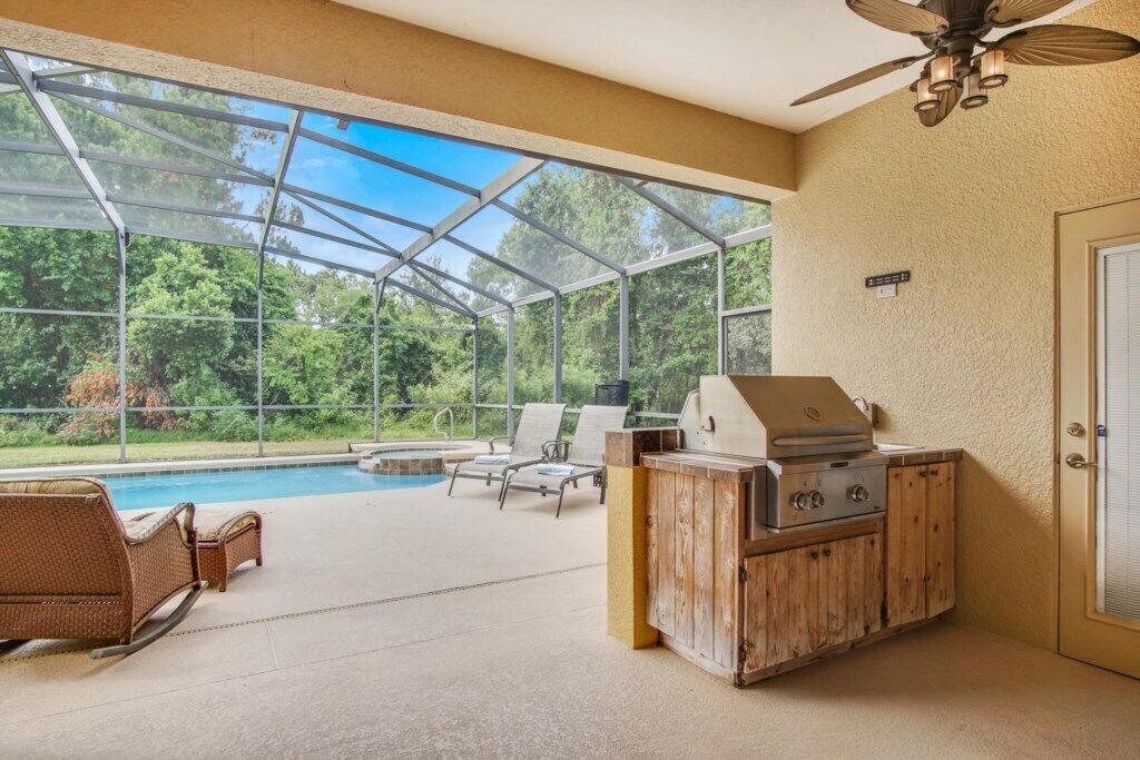 A covered outdoor area with a pool, lounge chairs, and a barbecue grill.