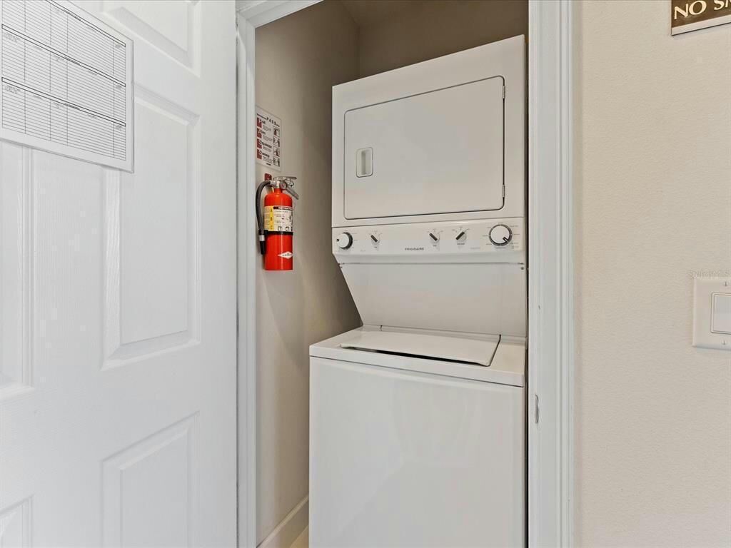 A laundry room with a white dryer and washing machine, a fire extinguisher, and a door with a vent.
