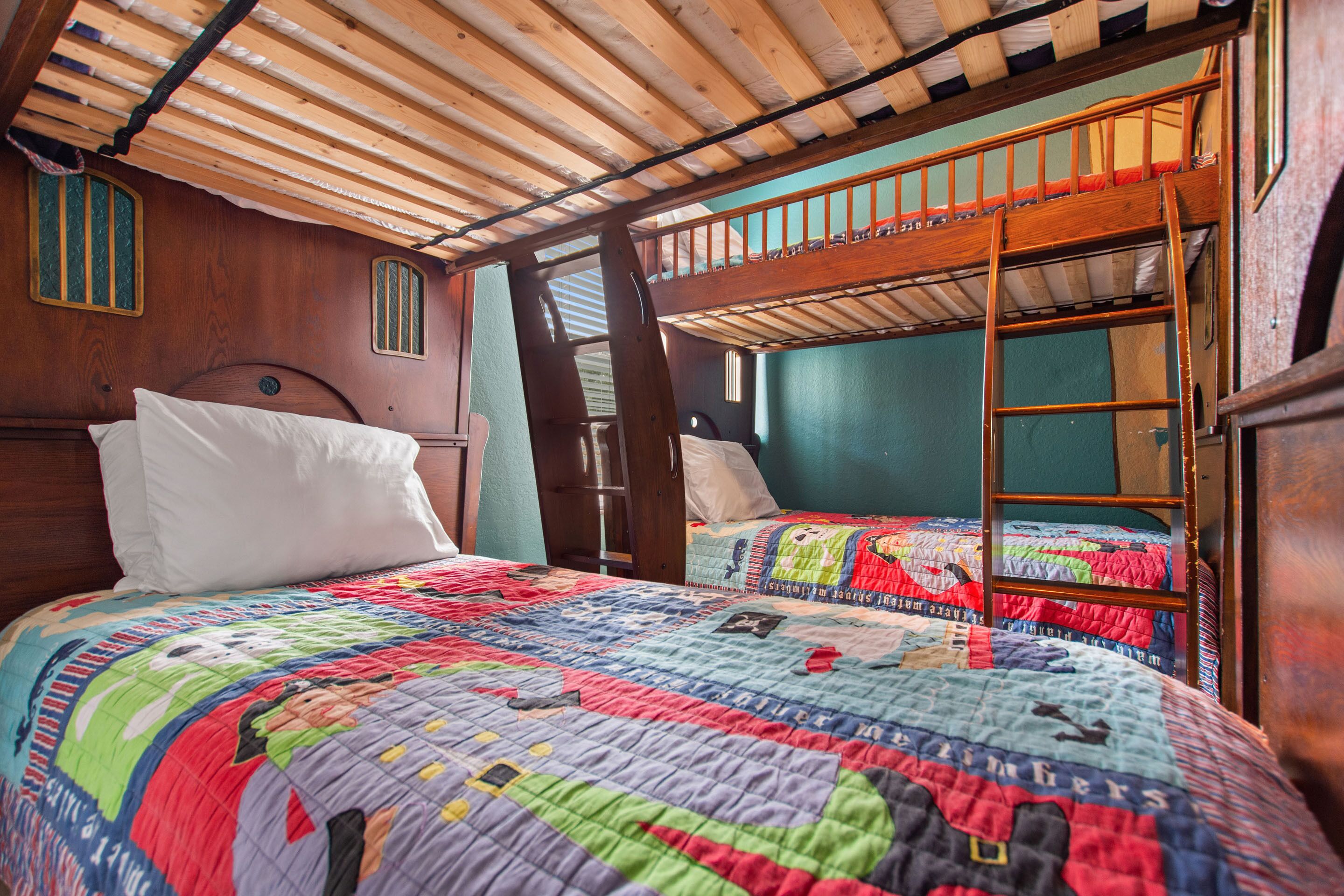 A bunk bed with a ladder, a wooden ceiling, and a colorful quilt.