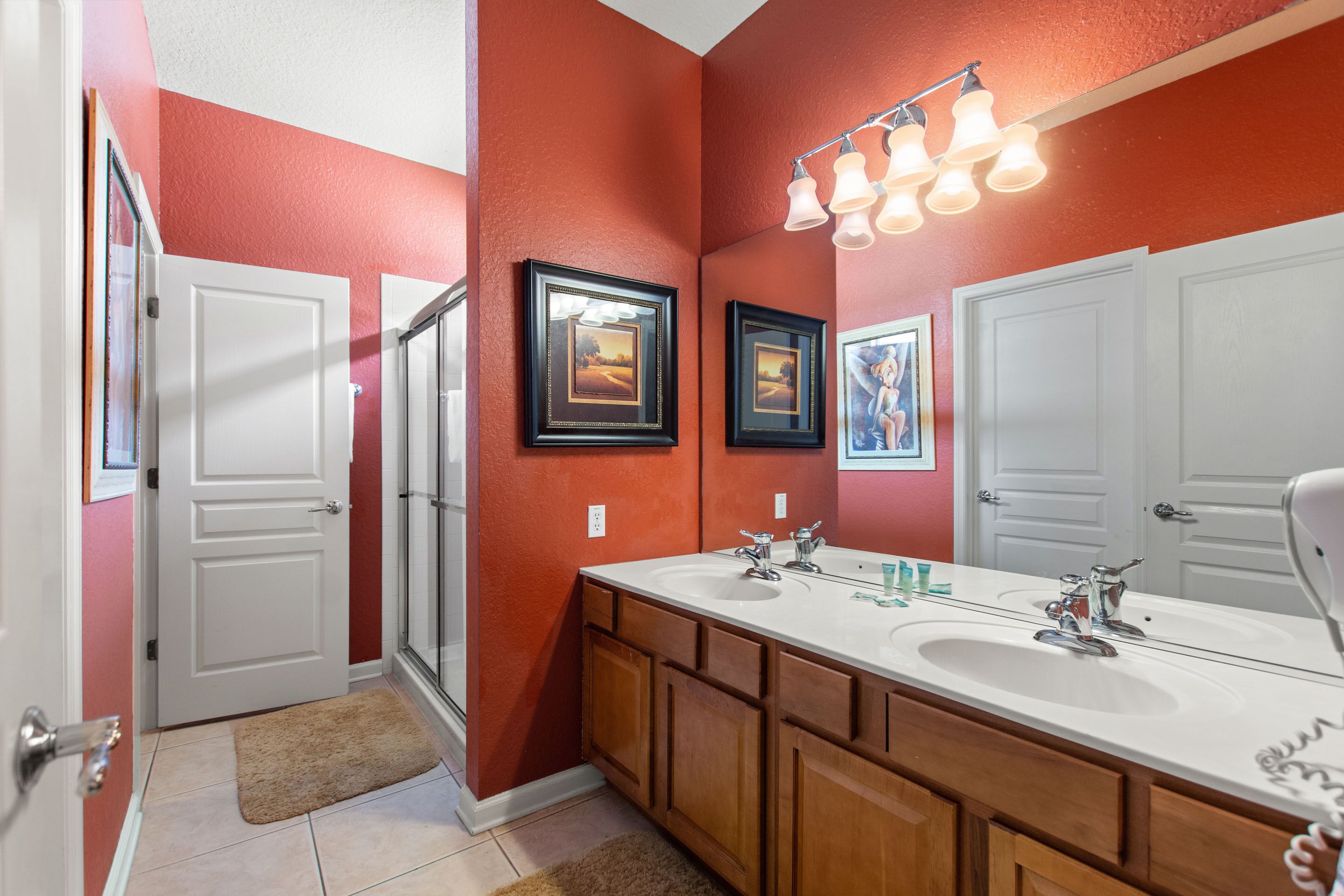 A bathroom with a double sink, wooden cabinets, and framed pictures on the wall.