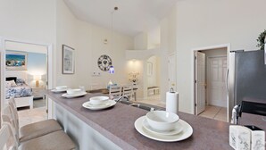 Une cuisine moderne dotée d’un îlot central, de meubles blancs et d’un coin repas avec une banquette et des chaises.