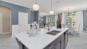 A modern kitchen with a large island, white countertops, and a stainless steel sink. - Fantasia @ Storey Lake by Shine Villas #408 (Kissimmee)