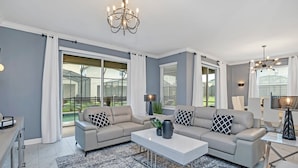 A modern living room with a sectional sofa, a coffee table, and a chandelier. - Fantasia @ Storey Lake by Shine Villas #408 (Kissimmee)