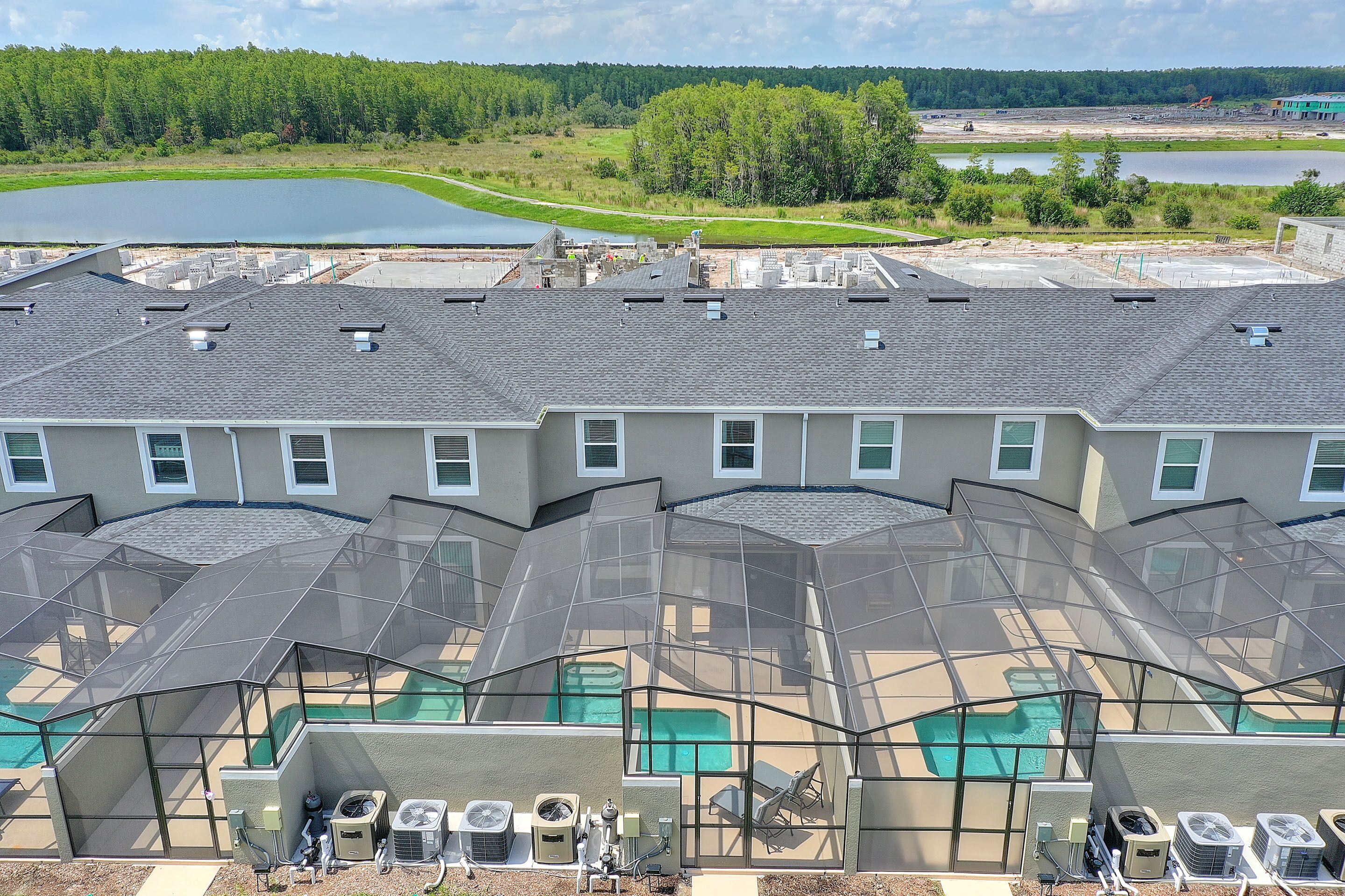 A multi-story building with a rooftop pool area, air conditioning units, and a view of a lake and forested area.