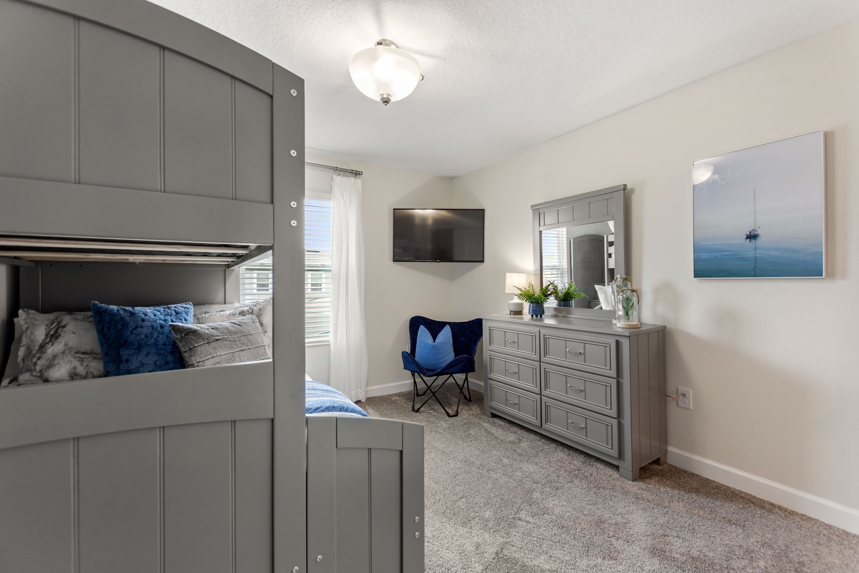 A bedroom with a bunk bed, a desk, a chair, a dresser, a TV, and a painting on the wall.