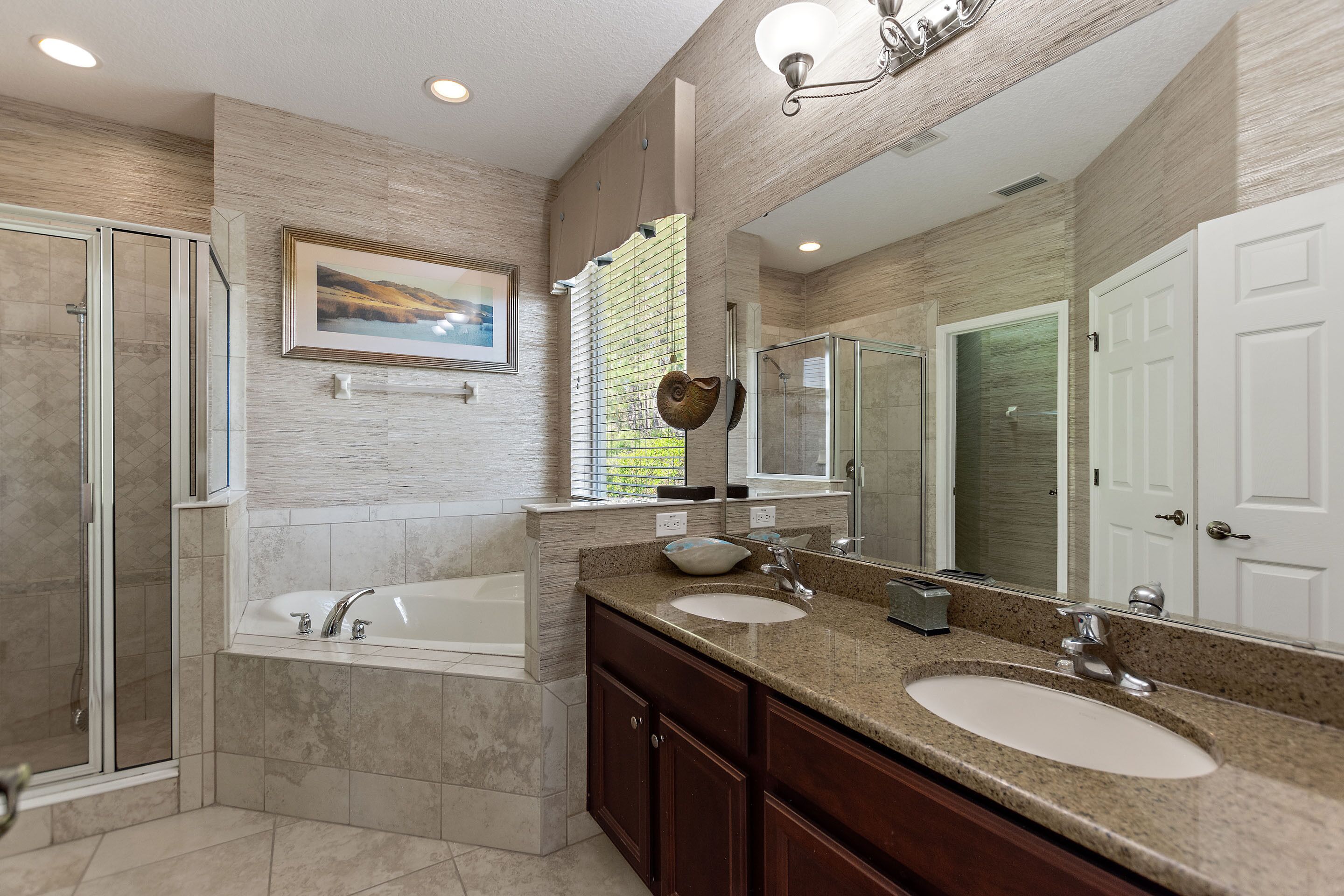A modern bathroom with a large mirror, two sinks, a bathtub, and a shower.