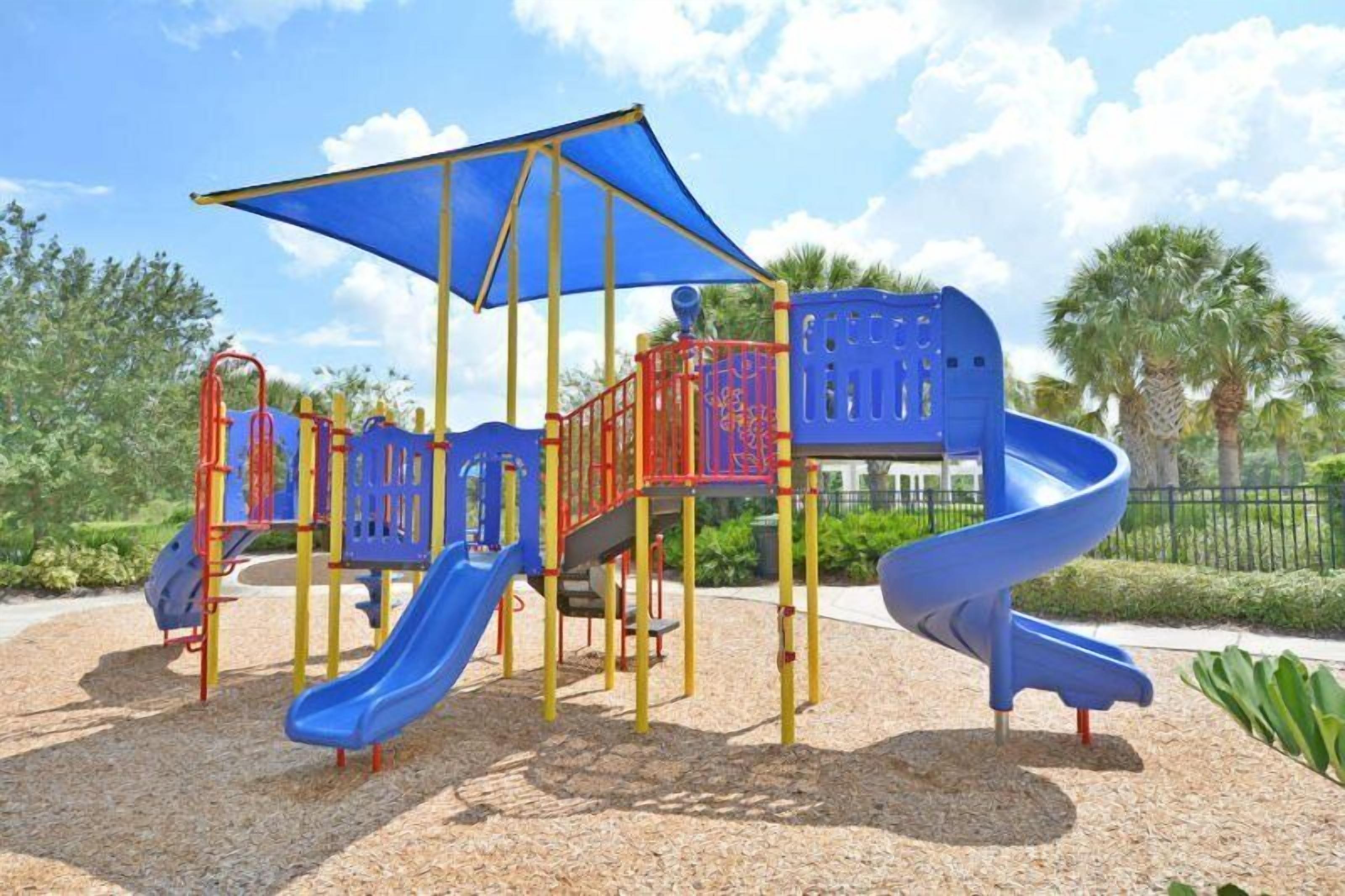 Une aire de jeux avec un toboggan bleu, des structures d’escalade rouges et bleues, et un auvent.