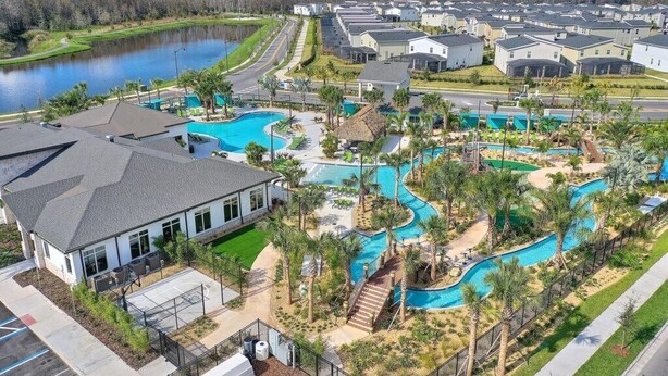 A residential area with a large swimming pool, multiple houses, and a lake in the background. - Jurassic Water View @storey Lake by Shine Villas! Sleeps up to 24! #021 (Kissimmee)