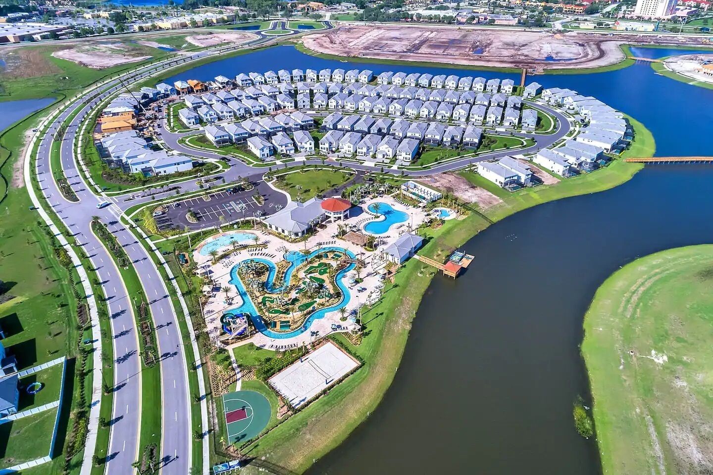 A residential area with a curved road, a swimming pool complex, and a large body of water.