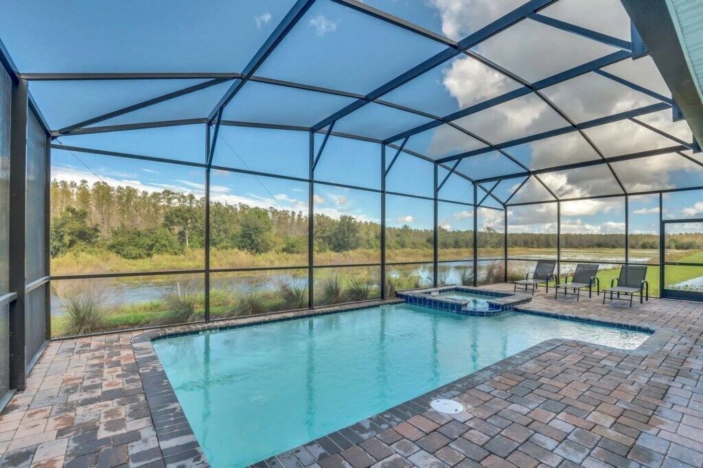 An outdoor swimming pool with a covered area, surrounded by a brick patio and a view of a natural landscape.