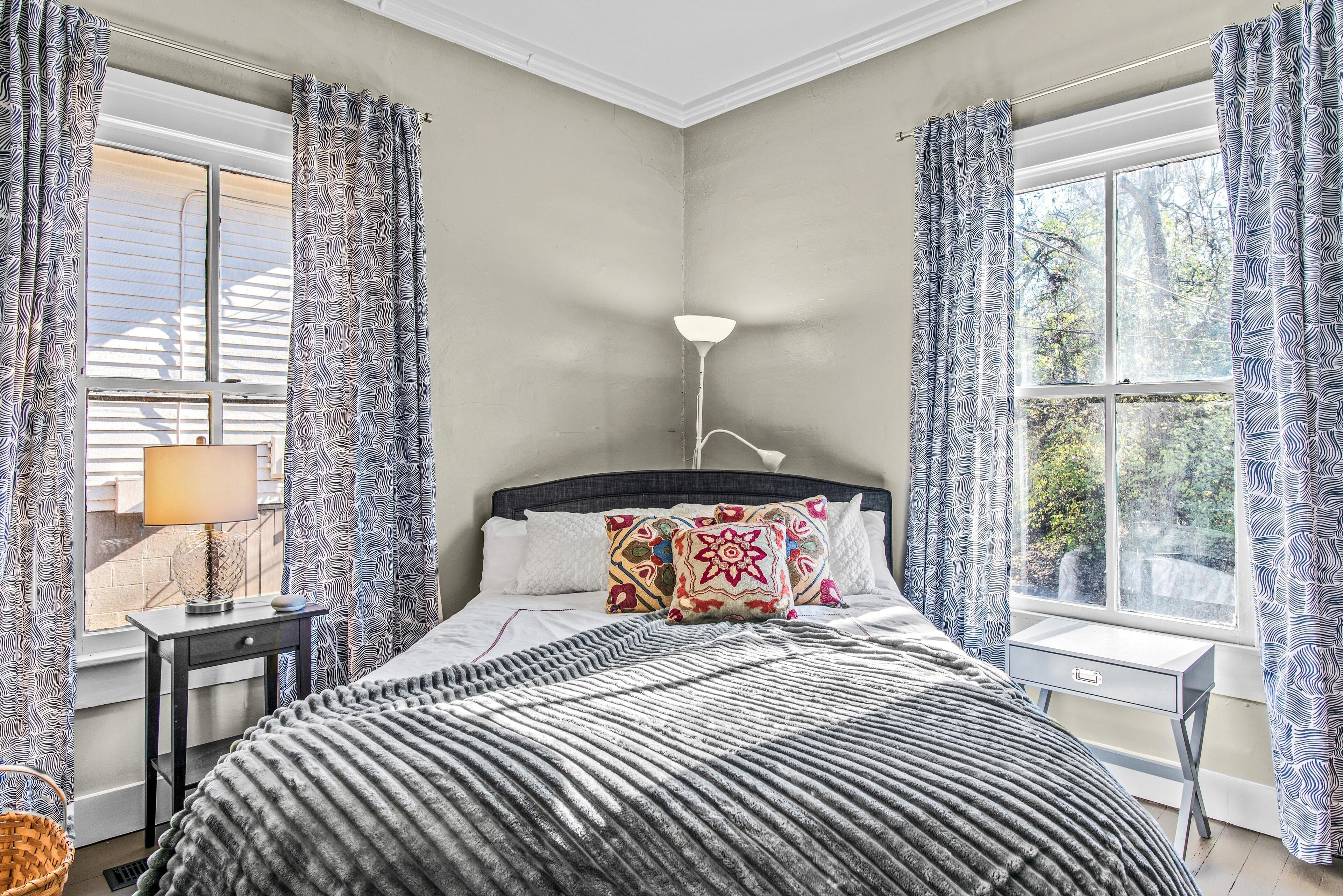 Een slaapkamer met een bed, nachtkastje, lamp en gordijnen.