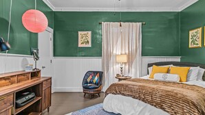 A bedroom with a green wall, a wooden desk, a colorful chair, a bed with a white and brown blanket, and a nightstand with a lamp. - Lenoir Cottage w/ covered patio and fire pit! (Athens)