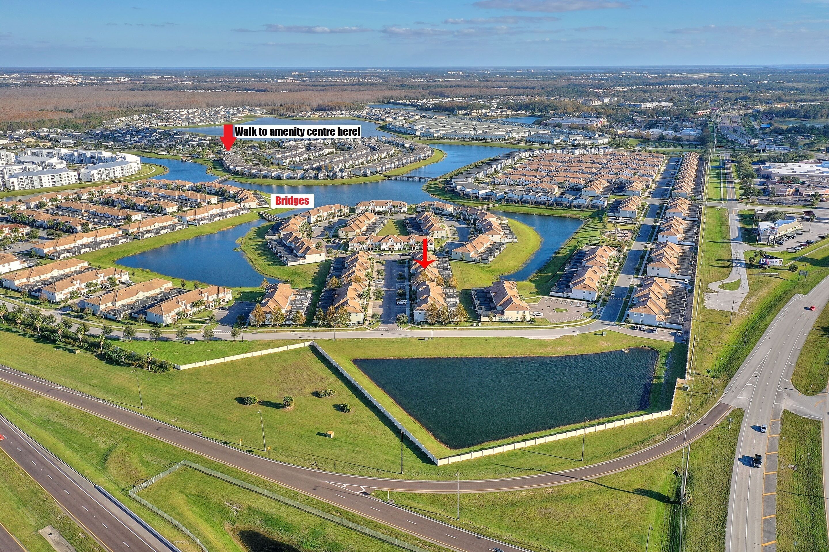 An aerial view of a residential area with a central park, a bridge, and a lake.