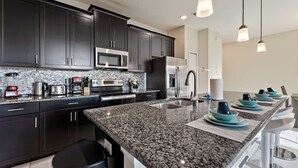 A modern kitchen with dark cabinets, granite countertops, stainless steel appliances, and bar stools.