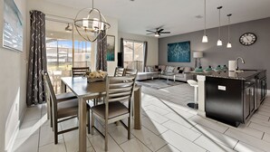 A modern kitchen with a central island, dining area with chairs, and a living room with a sofa and coffee table.