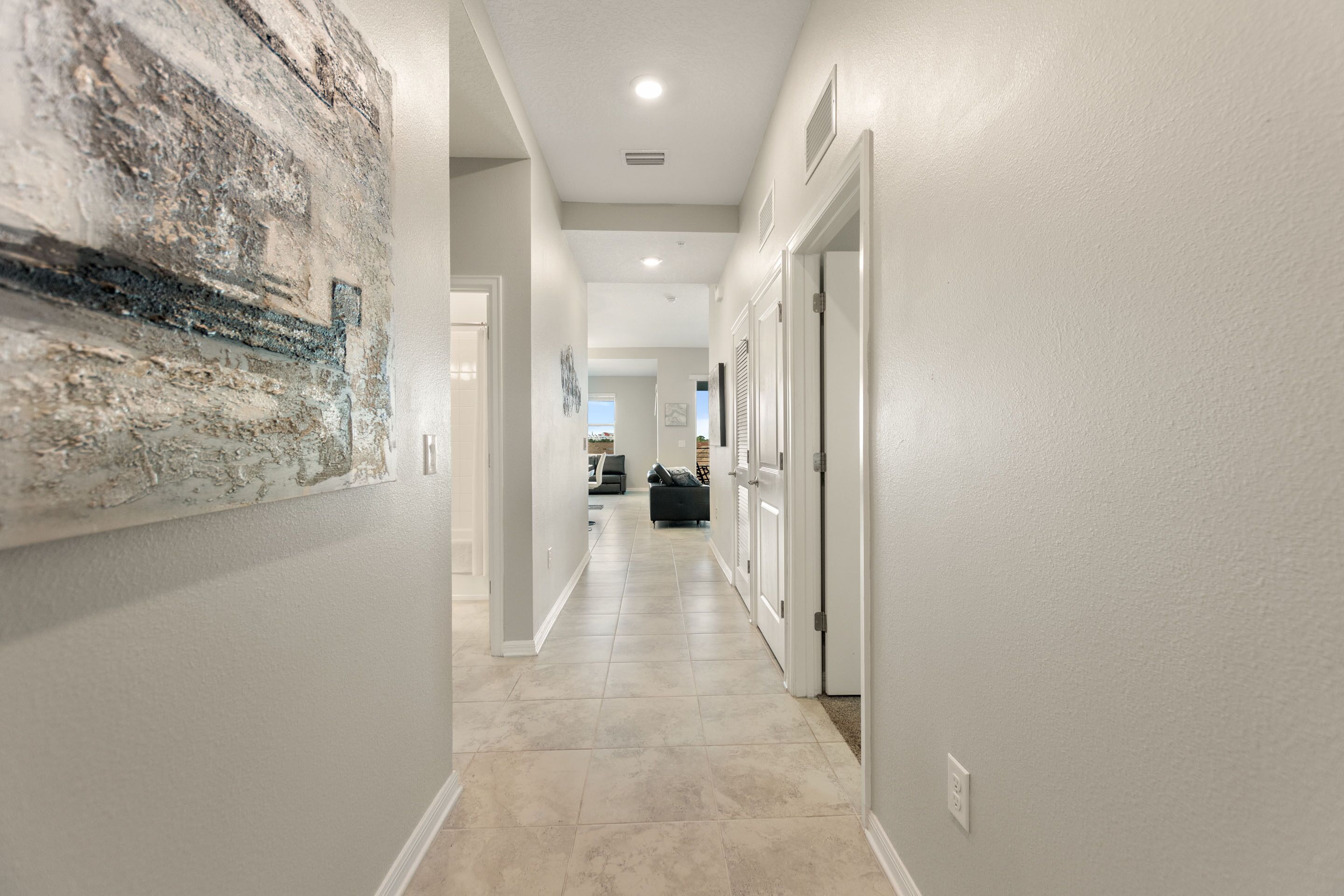 A hallway with a tiled floor, white walls, and a large abstract painting on the left.