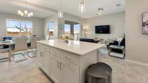 A spacious kitchen with a central island, pendant lighting, and a large window offering a view. - Fireworks @ Night -storey Lake by Shine Villas #709 (Kissimmee)