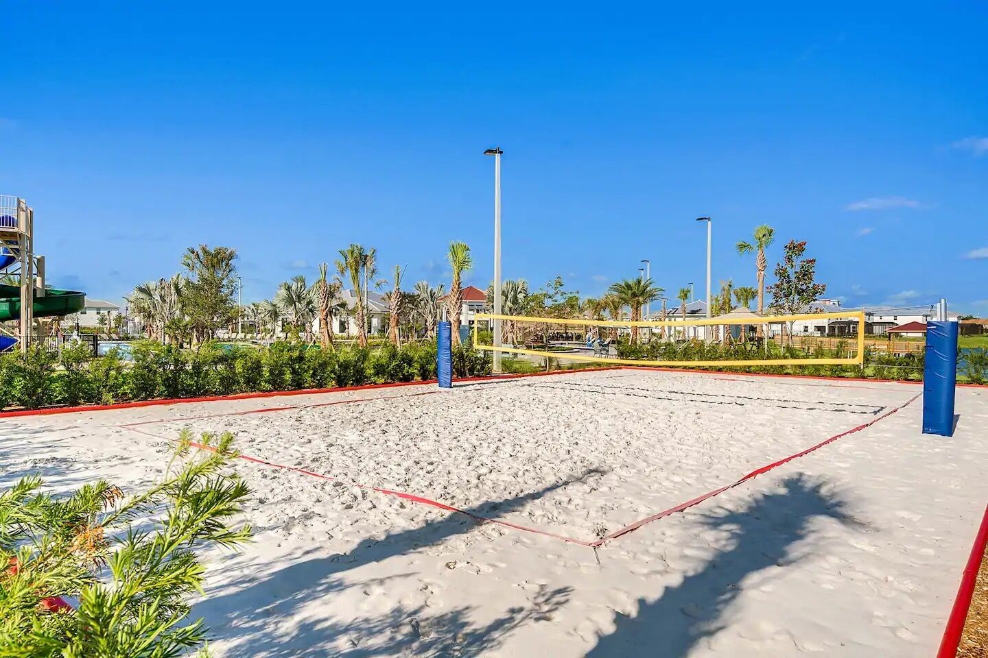Ein Beachvolleyballfeld mit Netz, umgeben von Palmen und einem Pool im Hintergrund.