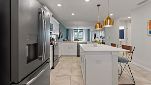 A modern kitchen with stainless steel appliances, a central island, pendant lighting, and a view to the dining area.