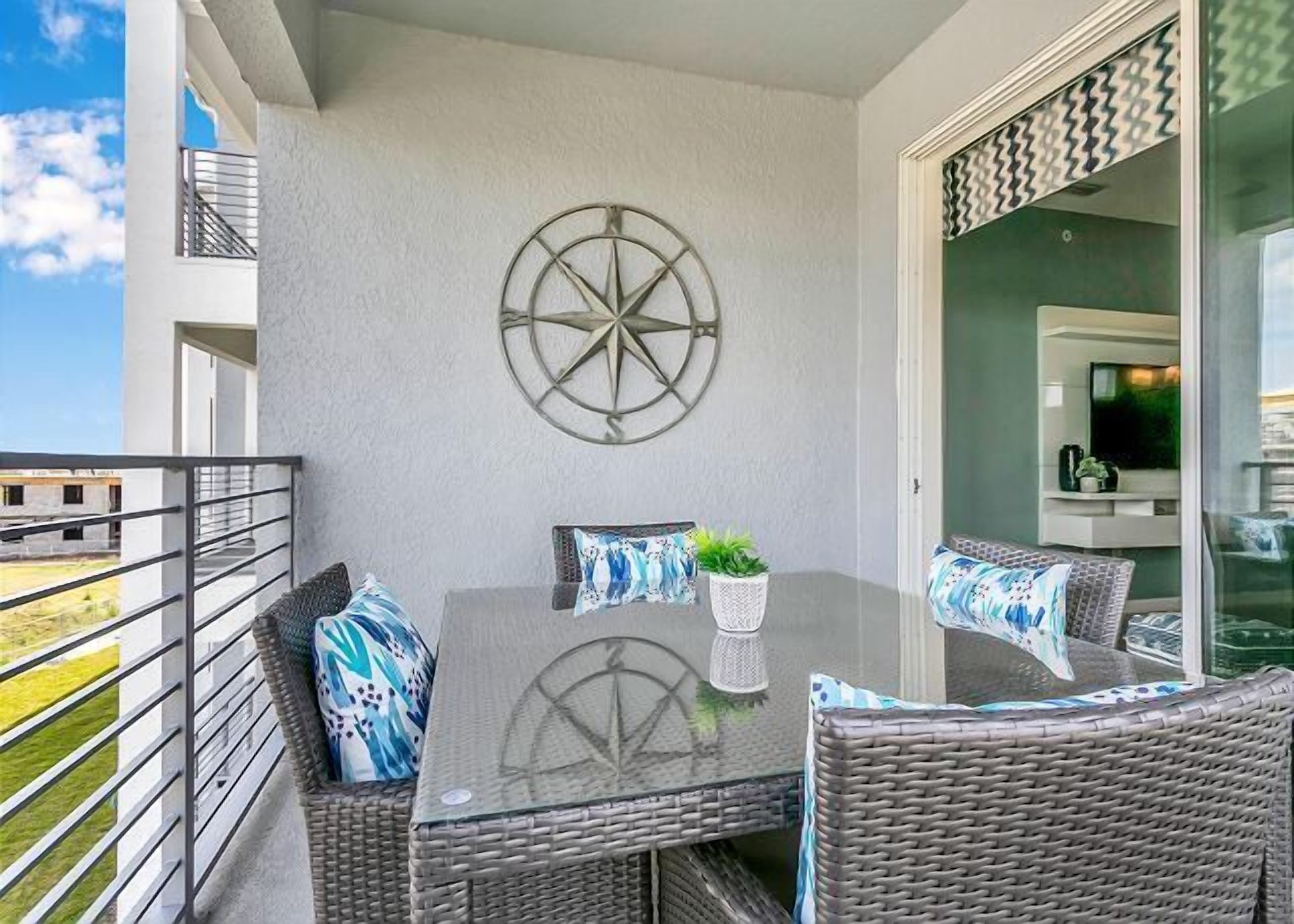 A balcony with a table and wicker chairs, a compass wall decoration, and a view of the surrounding area.